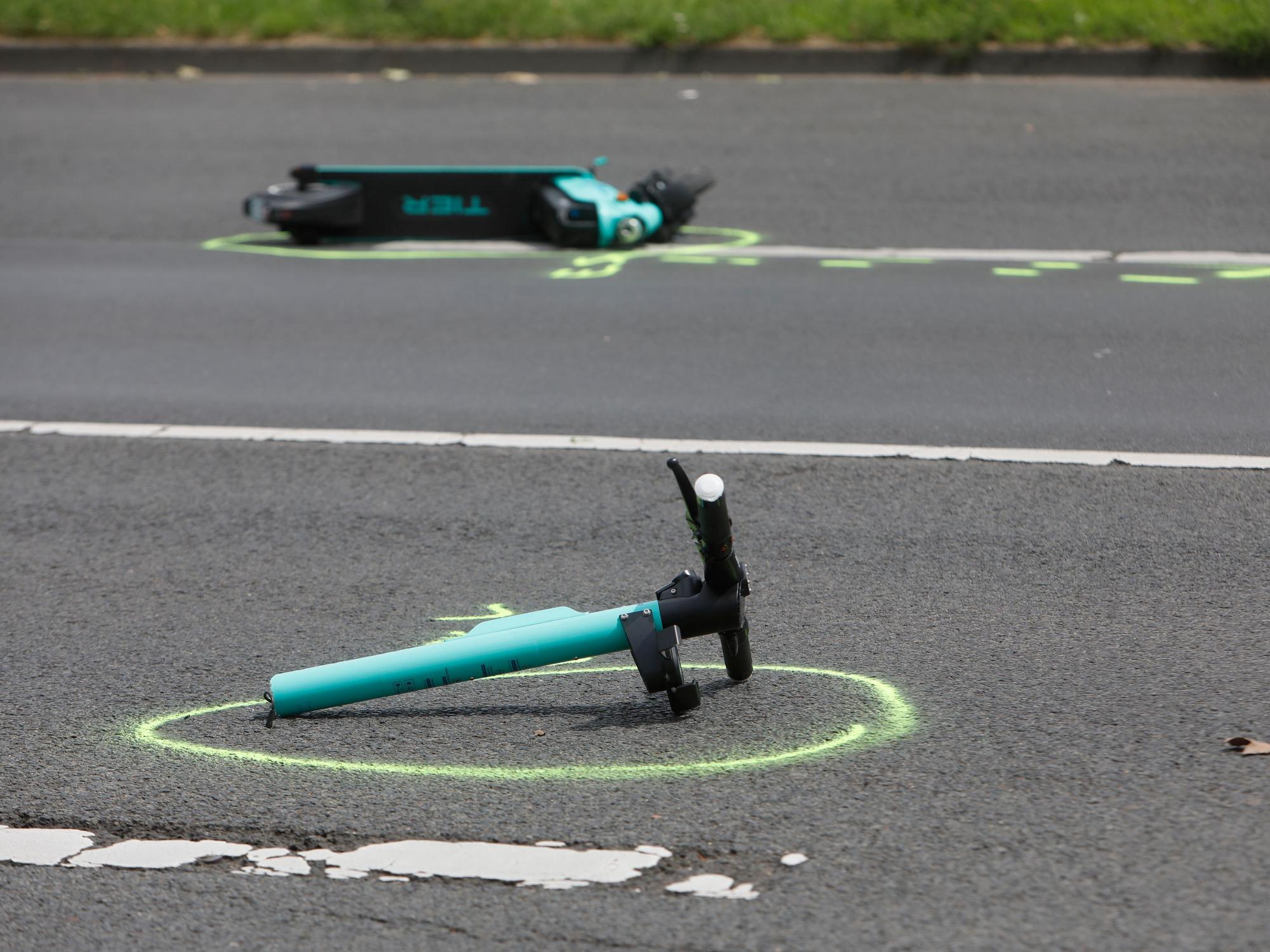 Ein in zwei Teile gerissener E-Scooter liegt auf einer Straße. Die Polizei hat beide Stelle mit Farbe markiert.