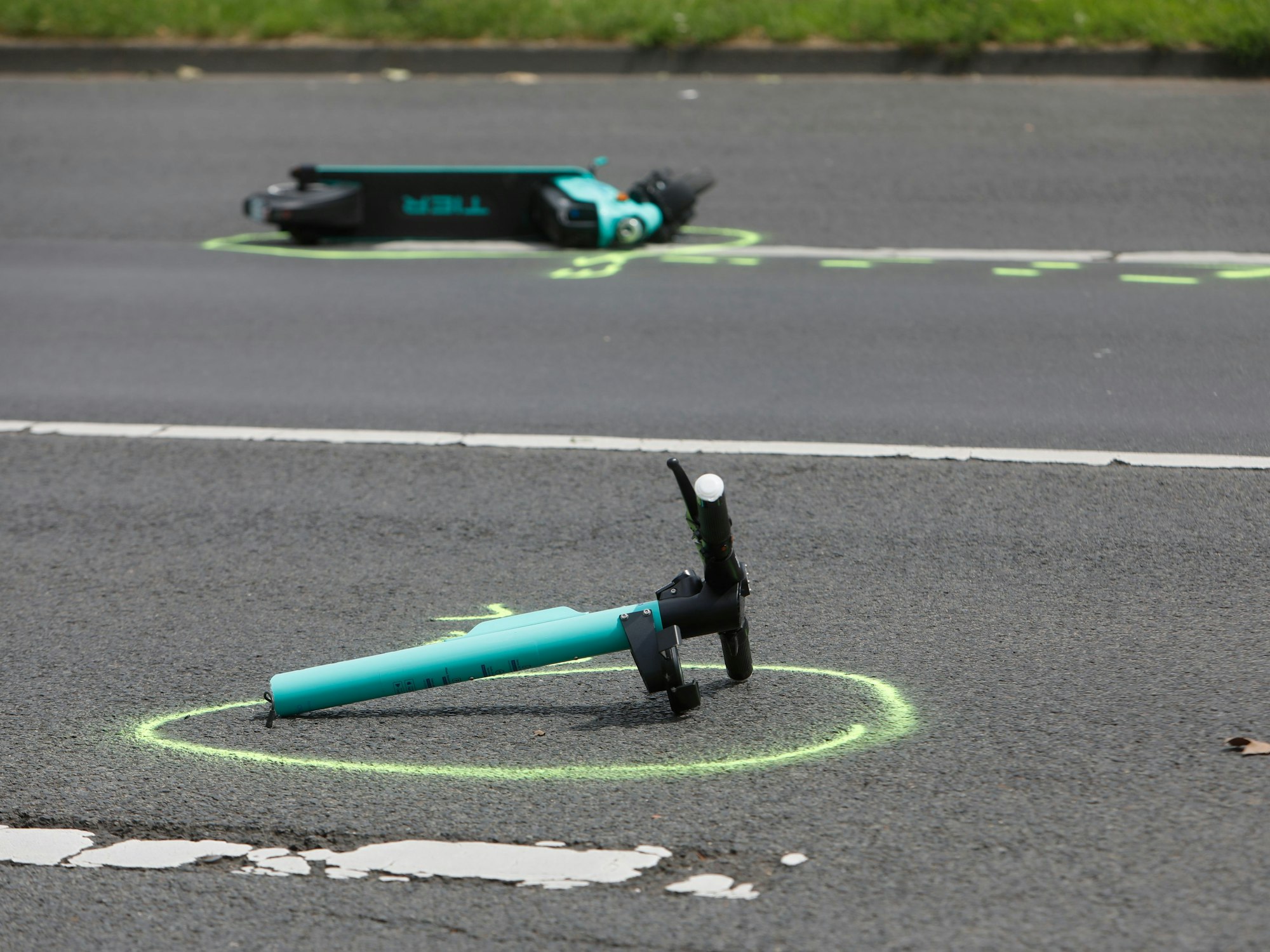 Ein in zwei Teile gerissener E-Scooter liegt auf einer Straße. Die Polizei hat beide Stelle mit Farbe markiert.