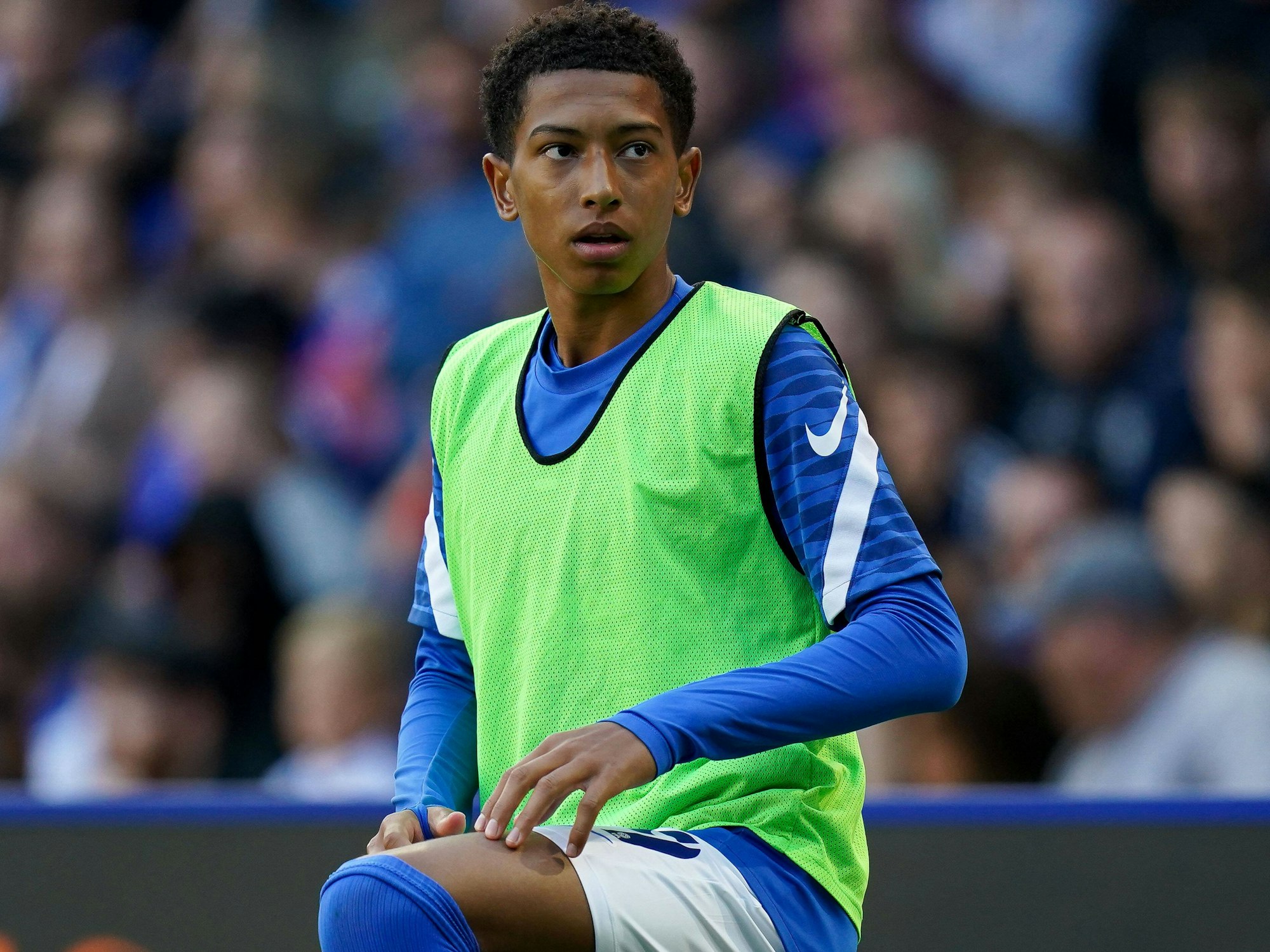 Jobe Bellingham kniet im Trainingsleibchen neben dem Platz und wärmt sich auf.