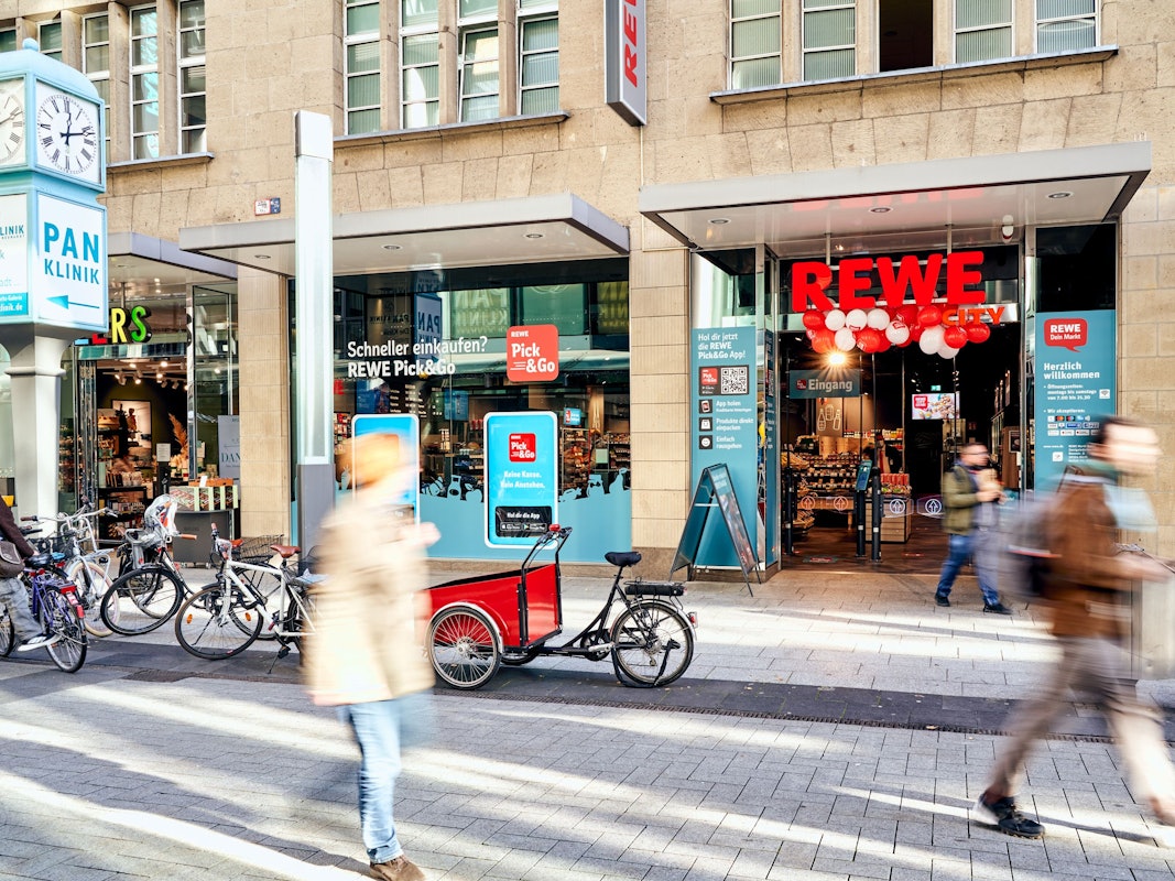 Menschen gehen am Rewe-Markt in der Zeppelinstraße in Köln vorbei.