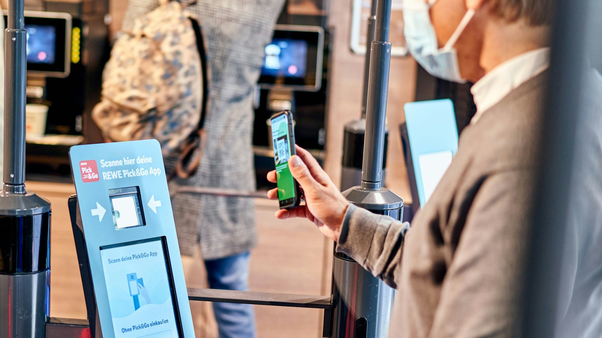 Hybrides Einkaufen bei Rewe: Ein Mann meldet sich am Eingang über einen QR-Code mit der Scan&Go-App an.