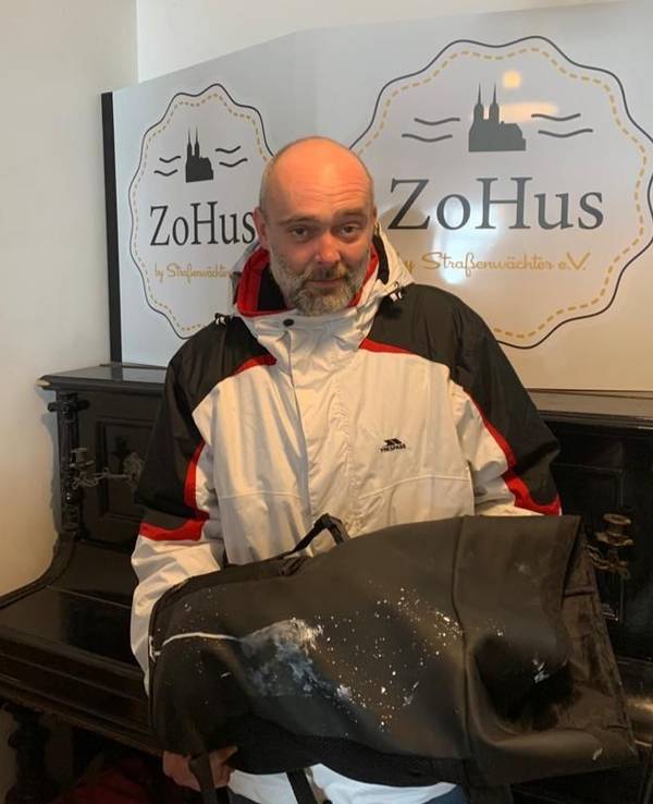 Der Obdachlose Robert steht in einem Lokal in Köln mit seinem beschmierten Rucksack.