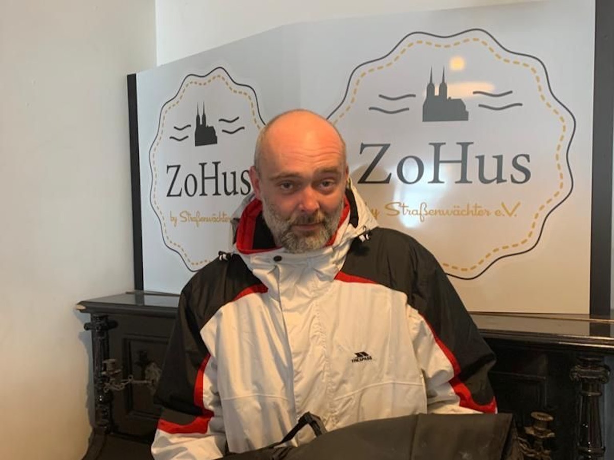 Der Obdachlose Robert steht in einem Lokal in Köln mit seinem beschmierten Rucksack.