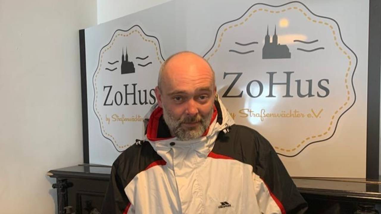 Der Obdachlose Robert steht in einem Lokal in Köln mit seinem beschmierten Rucksack.