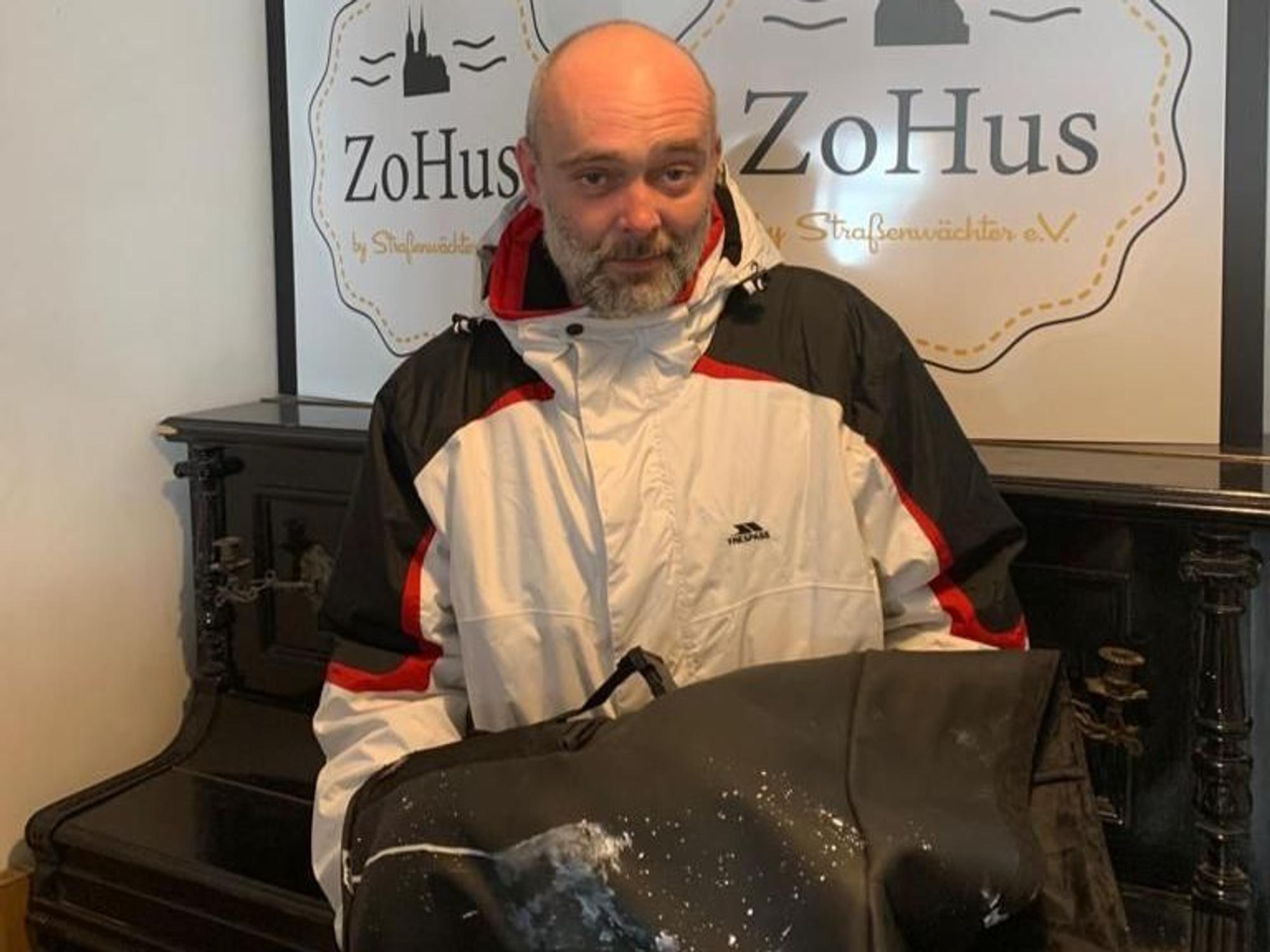 Der Obdachlose Robert steht in einem Lokal in Köln mit seinem beschmierten Rucksack.
