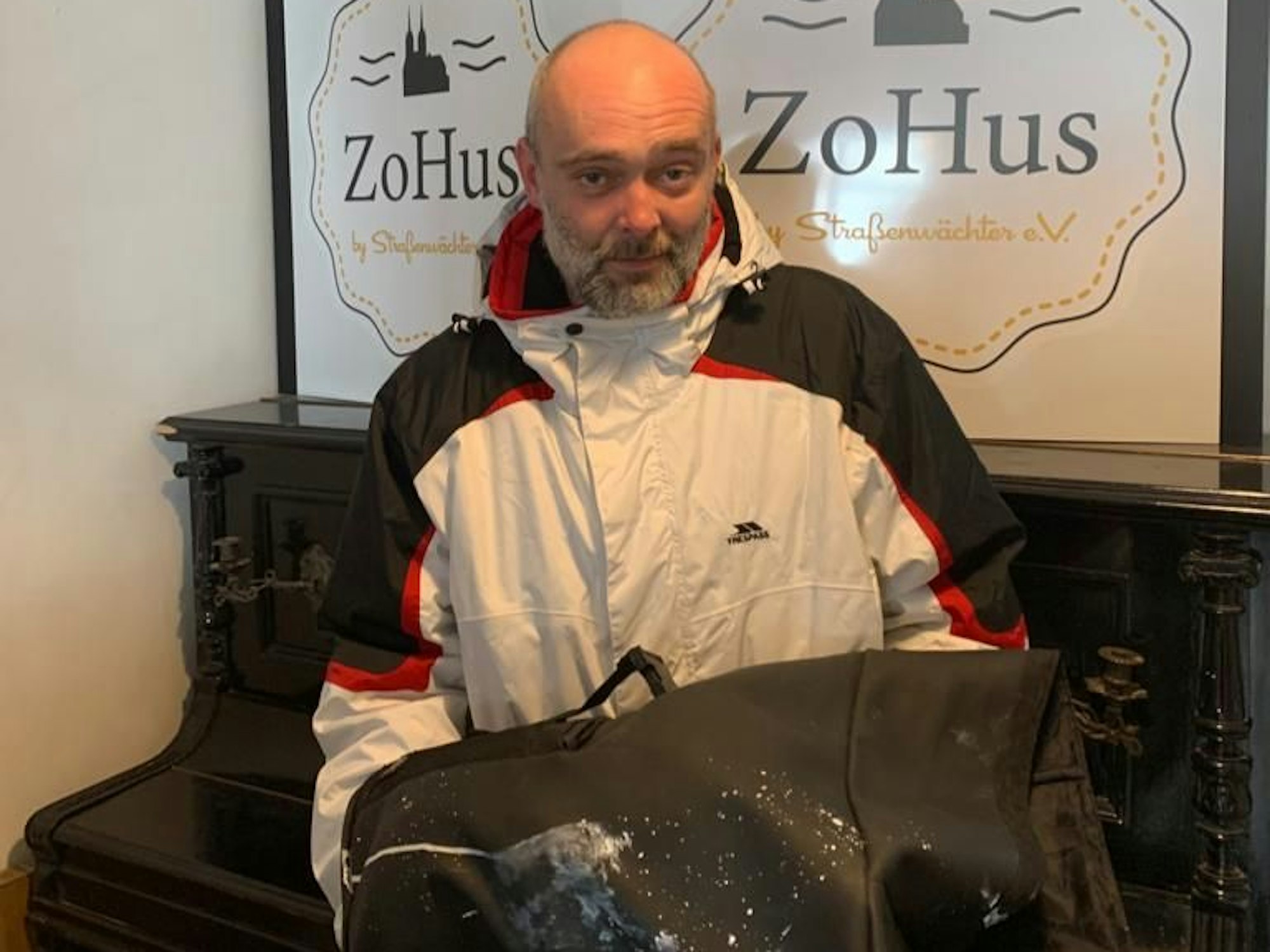 Der Obdachlose Robert steht in einem Lokal in Köln mit seinem beschmierten Rucksack.