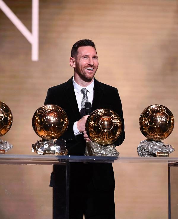 Lionel Messi steht vor einem Tisch mit dem sechsmal gewonnen Ballon d'Or.