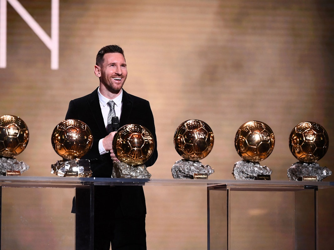 Lionel Messi steht vor einem Tisch mit dem sechsmal gewonnen Ballon d'Or.