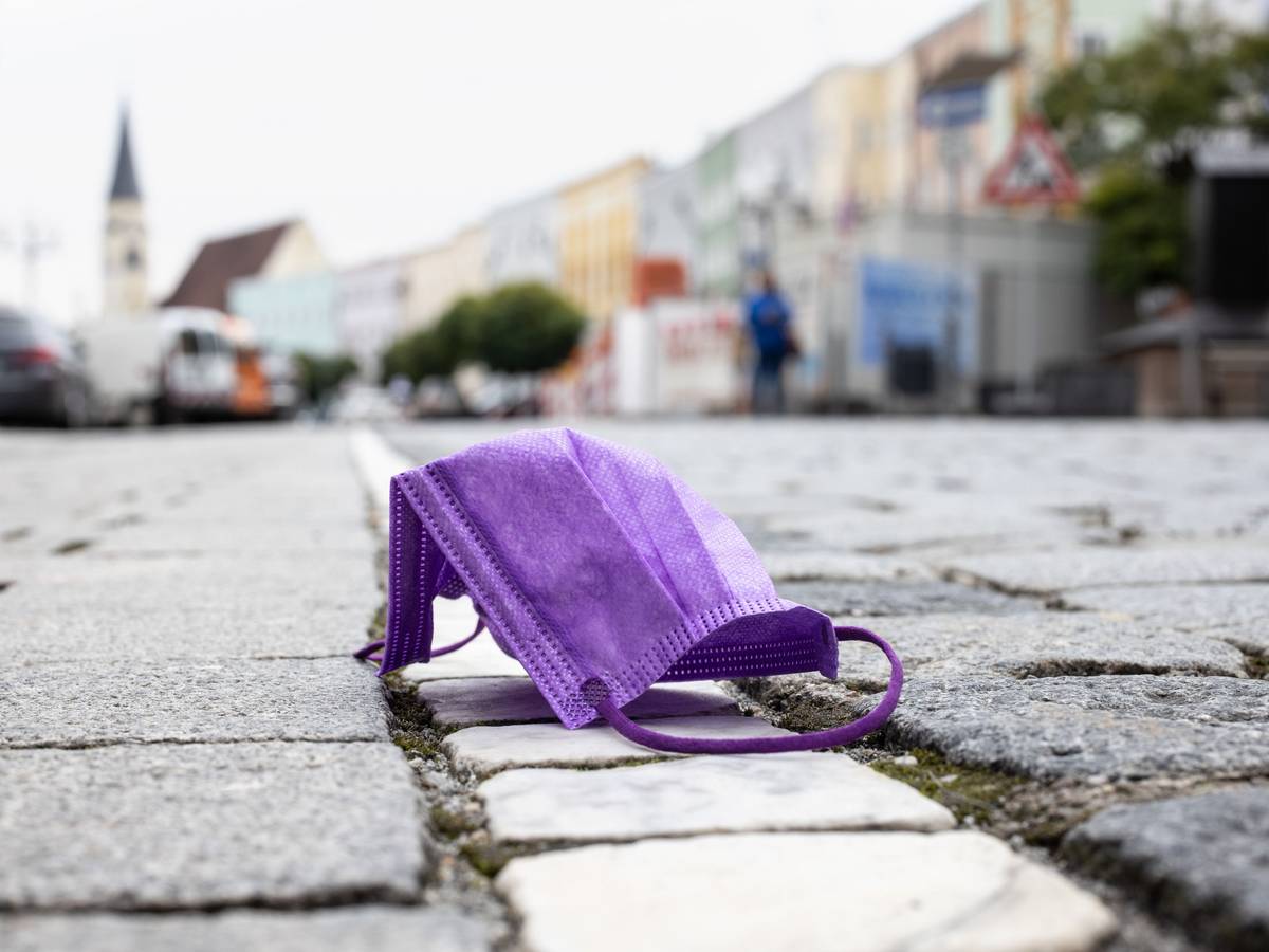 Bayern kämpft mit immer höher steigenden Corona-Zahlen. Auch die Bürger sind entzweit: Während die einen endlich lockerere Maßnahmen fordern, wollen die anderen härtere Maßnahmen, um die Infektionswelle einzudämmen. Auf dem Foto (aufgenommen am 26. Oktober 2021) zu sehen: Eine violette medizinische Maske, die auf einer Straße liegt, während im Hintergrund die Altstadt von Mühldorf am Inn zu sehen ist.