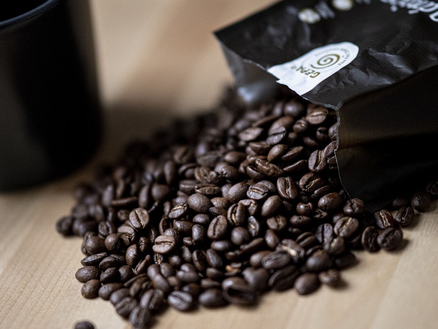 Guten Kaffee gibt es nicht überall. Doch woran erkennt man eigentlich guten Kaffee? Auf dem Symbolfoto (aufgenommen am 24. September 2021) liegen Kaffeebohnen neben einer Tasse auf einem Tisch.