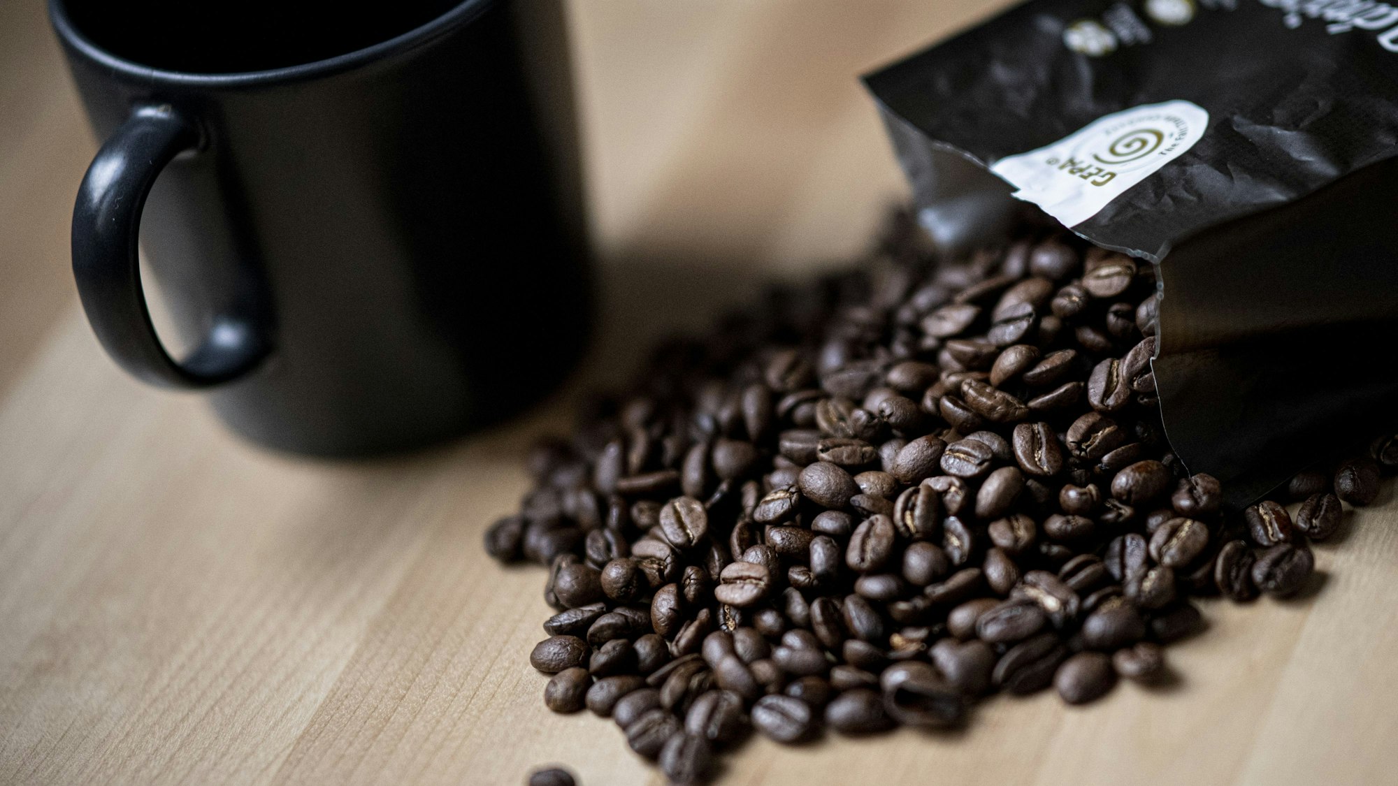 Guten Kaffee gibt es nicht überall. Doch woran erkennt man eigentlich guten Kaffee? Auf dem Symbolfoto (aufgenommen am 24. September 2021) liegen Kaffeebohnen neben einer Tasse auf einem Tisch.