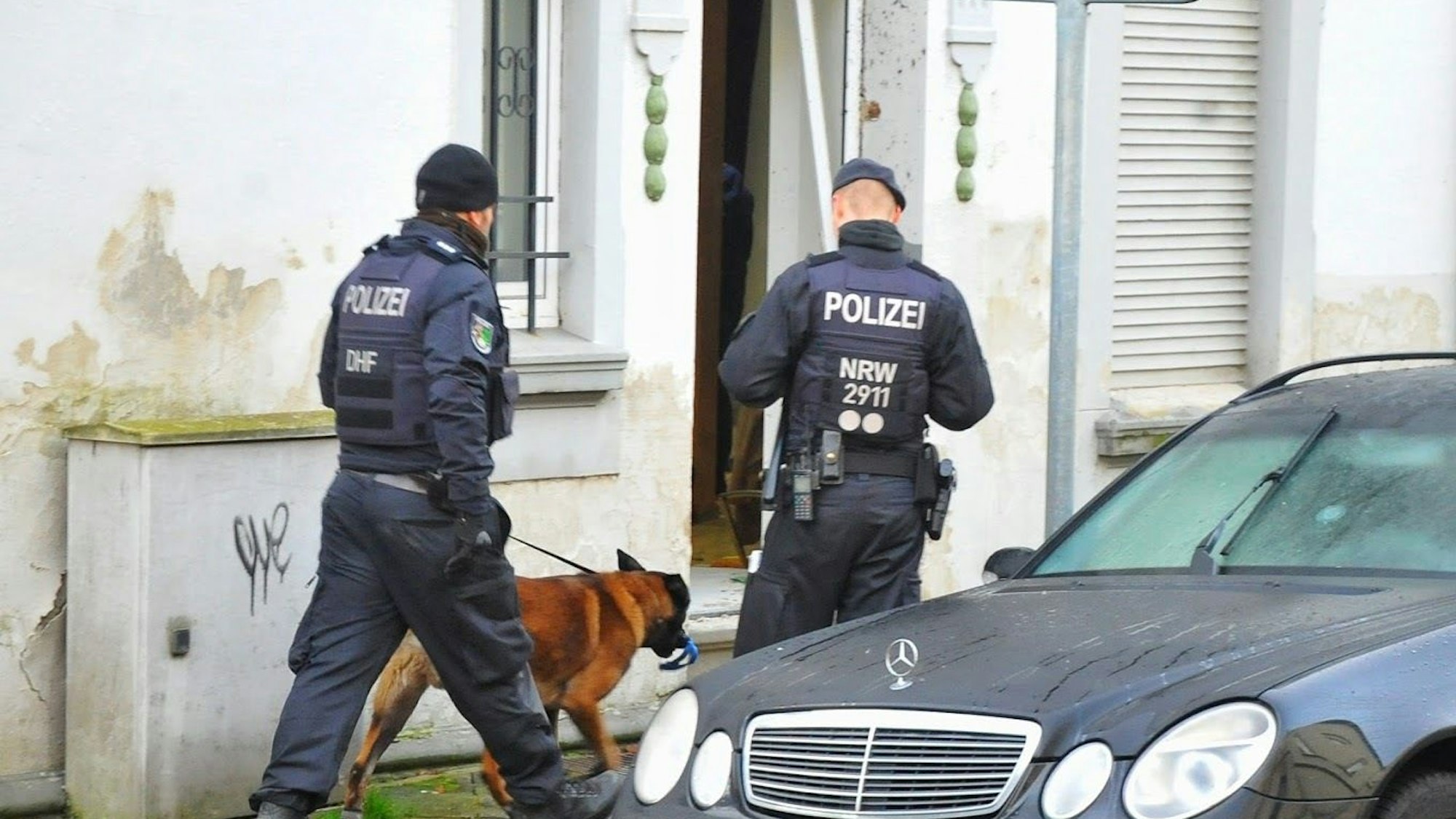 Mönchengladbach: Polizisten und ein Spürhund stehen vor einem Haus.