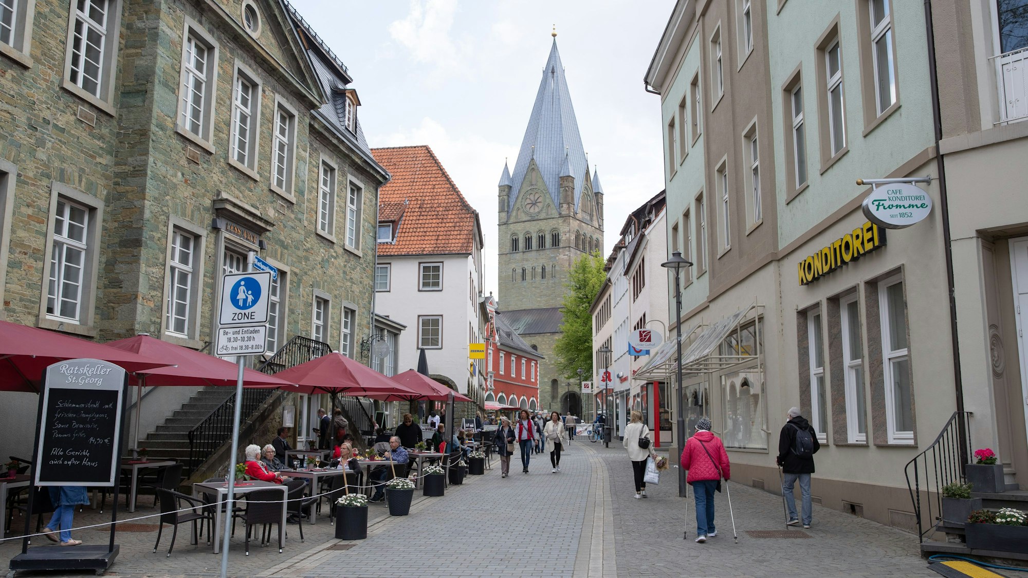 Gäste sitzen vor dem Ratskeller in Soest an der Rathausstraße. Im Hintergrund ist der St.Patrokli-Dom zu sehen.