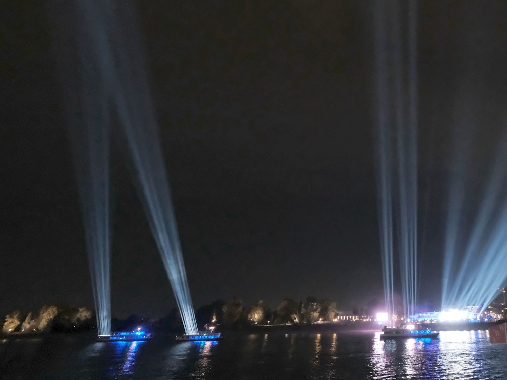 Was für eine Strahlkraft! Schiffe machen am 29. Oktober 2021 auf dem Rhein bei Köln auf das 401-jährige Firmen-Jubiläum von DuMont aufmerksam und lassen den Himmel erleuchten.