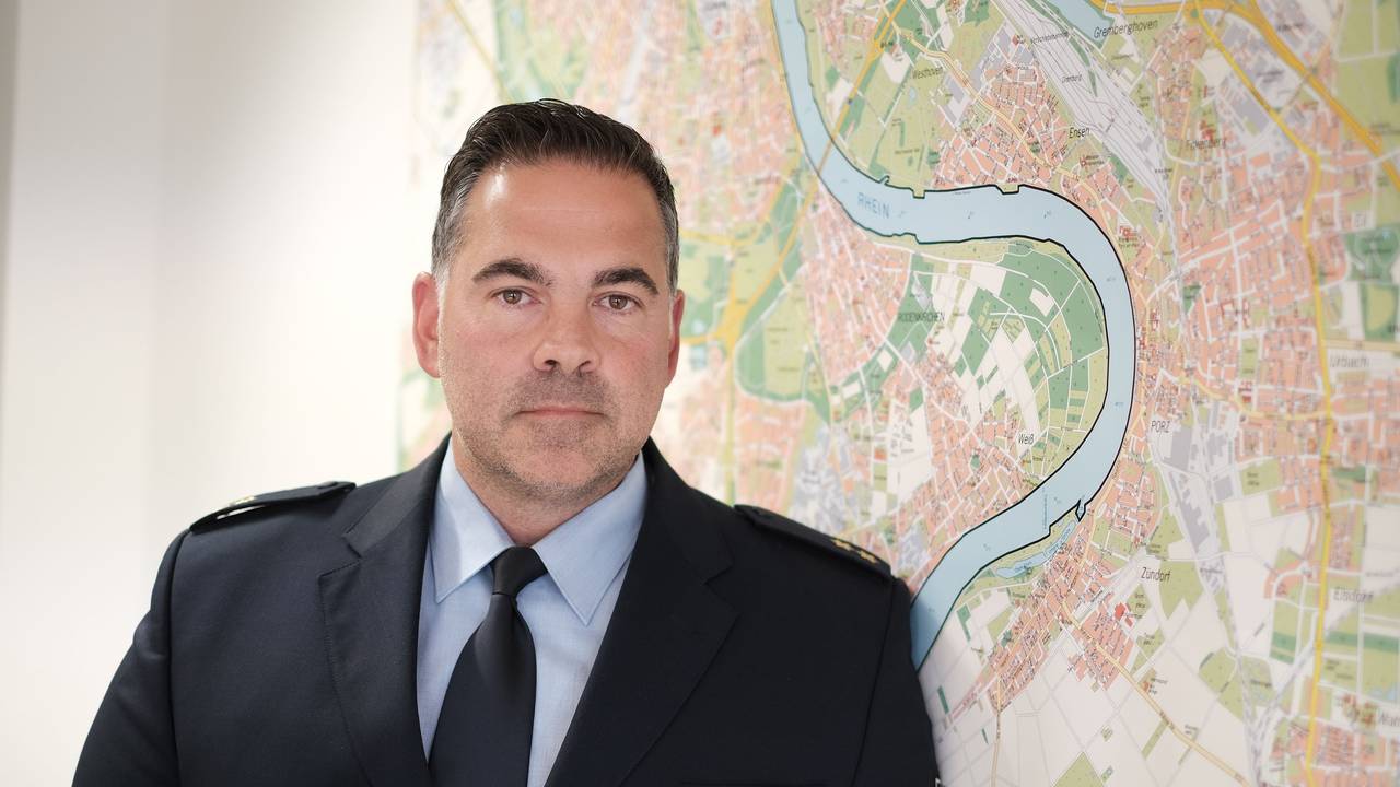 Michael Plagge blickt in die Kamera, hinter ihm der Stadtplan von Köln