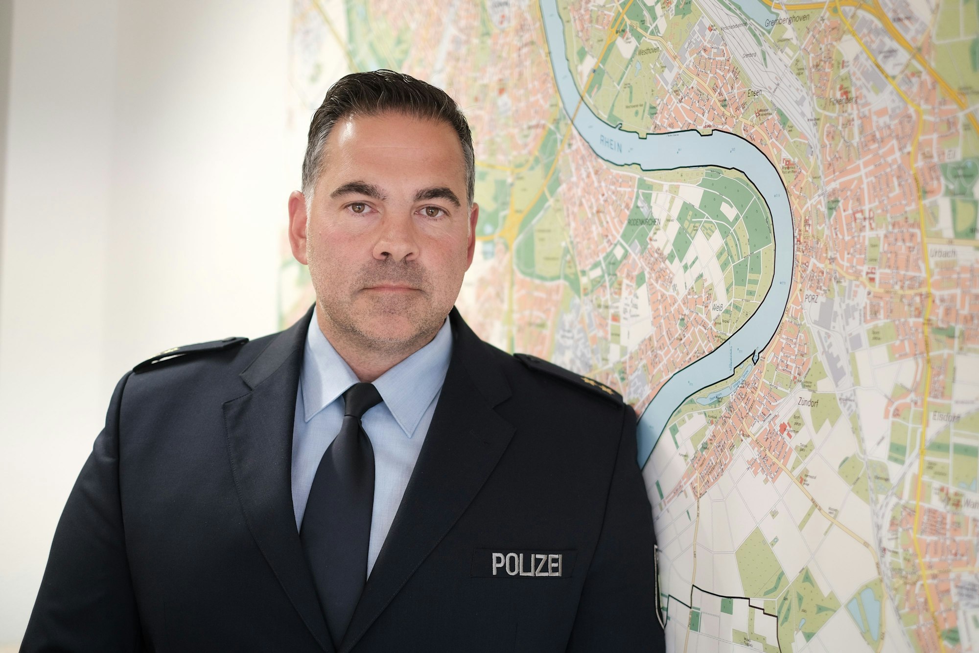Michael Plagge blickt in die Kamera, hinter ihm der Stadtplan von Köln