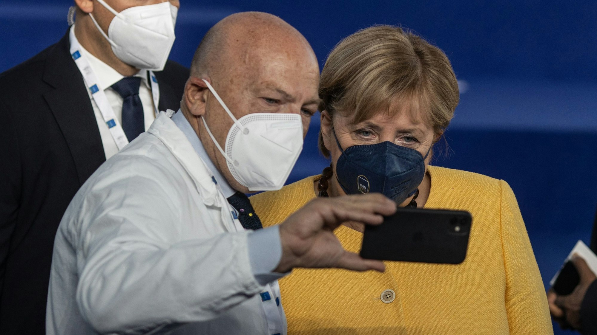 Ein Mitarbeiter des Gesundheitswesens macht ein Selfie mit der geschäftsführenden Bundeskanzlerin Angela Merkel (CDU,r) während sie sich für ein gemeinsames Gruppenfoto aufstellen.