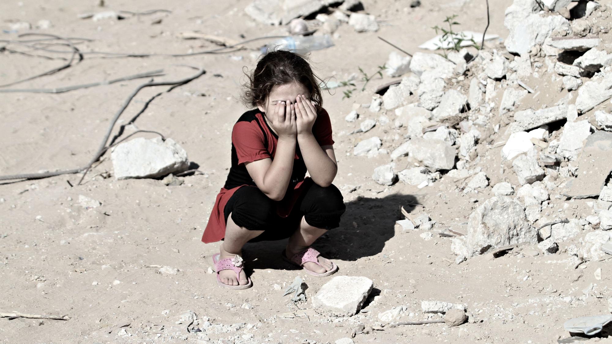 Das Symbolfoto (aufgenommen am 14. September 2014) zeigt ein Mädchen in den Ruinen von Shejaiya. Sie kauert auf dem Boden und hält sich die Hände vors Gesicht.