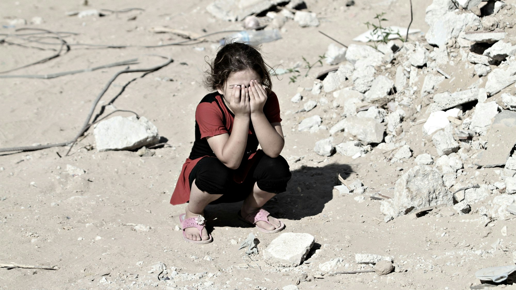 Das Symbolfoto (aufgenommen am 14. September 2014) zeigt ein Mädchen in den Ruinen von Shejaiya. Sie kauert auf dem Boden und hält sich die Hände vors Gesicht.
