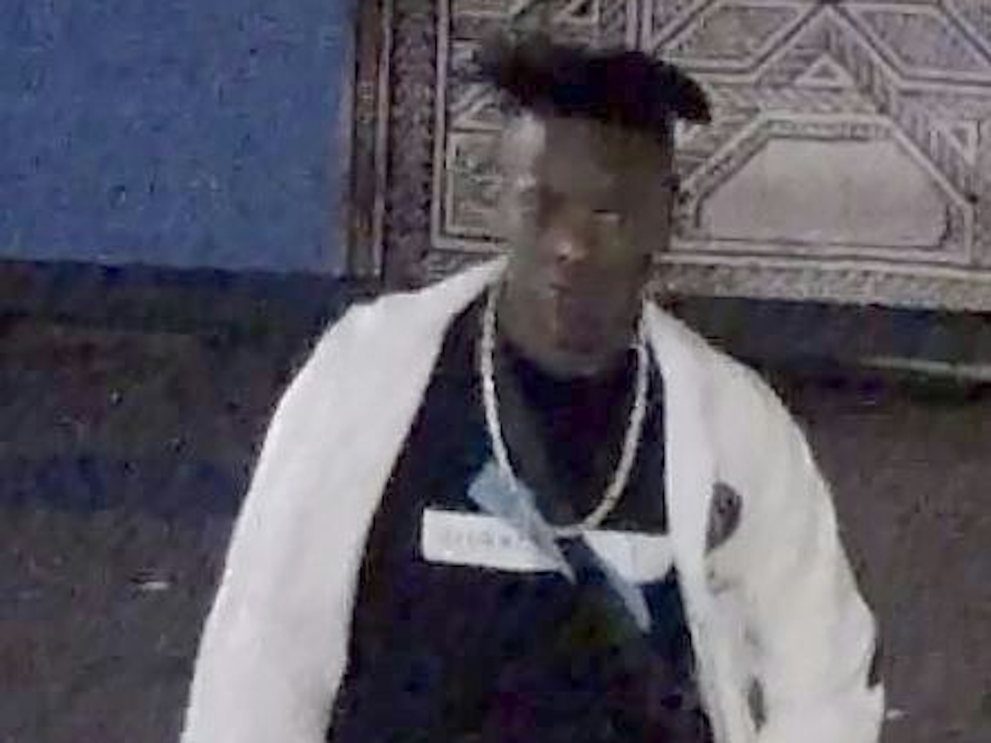 Der Tatverdächtige trägt eine weiße Joggingjacke, über einem dunklen Shirt hängt eine auffällige Silberkette.