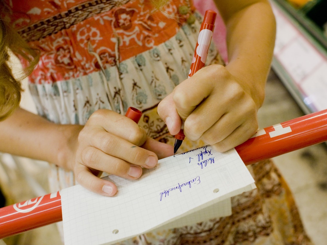 ARCHIV - Ein linkshändiges Mädchen kauft mit einem Einkaufszettel in einem Supermarkt ein und hakt mit einem Stift die Waren ab.