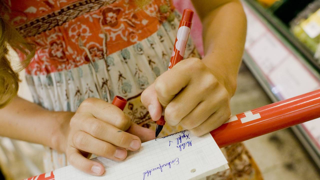 ARCHIV - Ein linkshändiges Mädchen kauft mit einem Einkaufszettel in einem Supermarkt ein und hakt mit einem Stift die Waren ab.