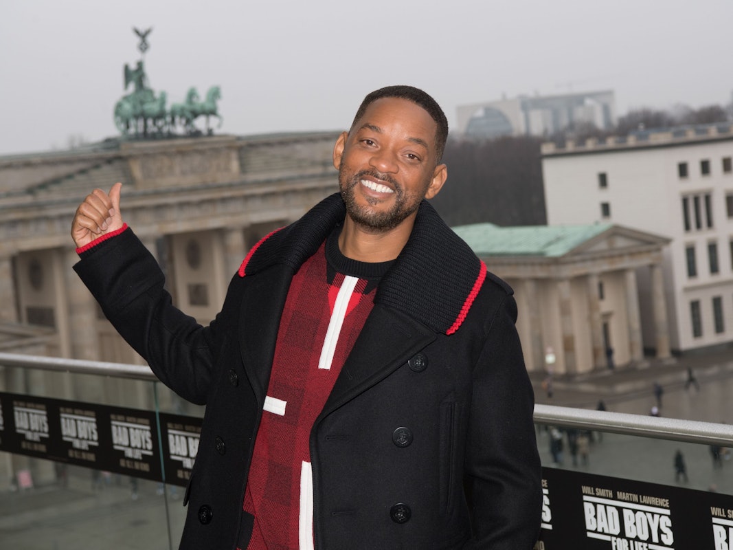 Der Schauspieler Will Smith steht vor dem Brandenburger Tor und lächelt.