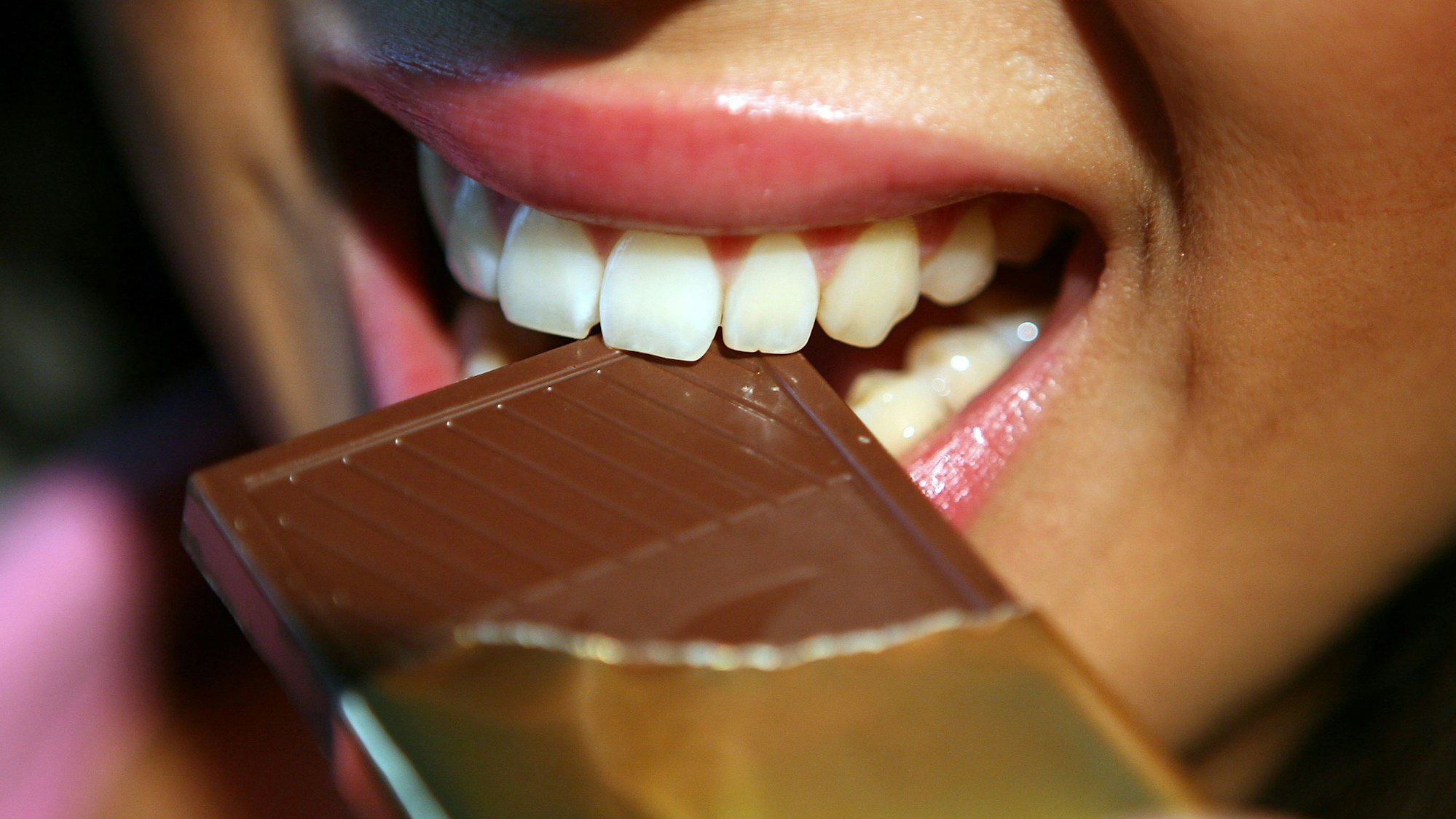 Weil sie Glasstücke enthalten können, wurden Riegel von „Max Balance Sport Protein Bar“ in der Geschmacksrichtung Schoko-Brownie zurückgerufen. Das Symbolbild zeigt eine Frau, die in einen Schokoriegel beißt. Das Foto steht nicht im Zusammenhang mit dem Rückruf.