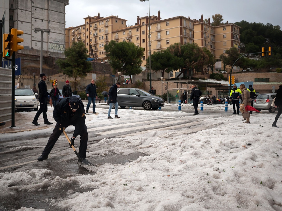 Ein Polizist räumt nach einem schweren Hagelsturm in der Innenstadt von Malaga den Hagel von der Straße. Das Sturmtief «Gloria» hat in Spanien große Schäden hinterlassen.