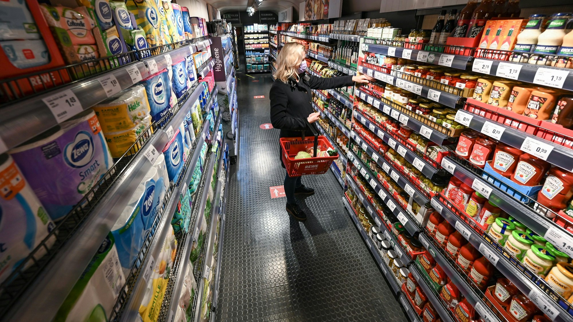 Eine Frau steht bei der Vorstellung des temporären Projekts "Fairer Supermarkt im Zug" im Frankfurter Hauptbahnhof mit einem Einkaufskorb vor einem Lebensmittelregal.