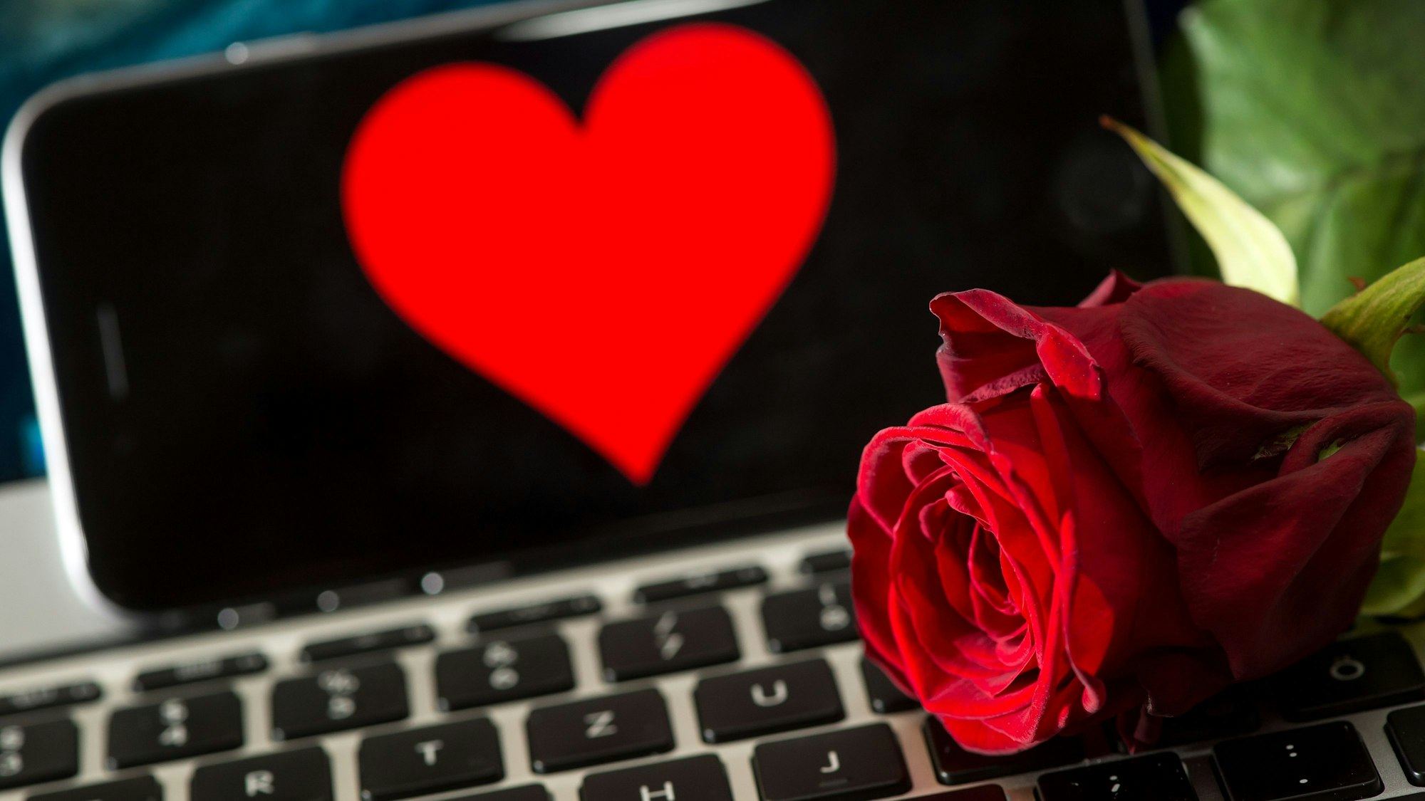 Online-Dating generell ist nicht einfach, doch vor allem gläubige Menschen haben Schwierigkeiten dabei, einen Partner zu finden. Extra Dating-Apps sollen dabei helfen. Das Symbolfoto (aufgenommen am 20. April 2016) zeigt eine Rose, die auf einer Computertastatur liegt. Im Hintergrund ist ein Smartphone zu sehen, auf dem ein Herz abgebildet ist.