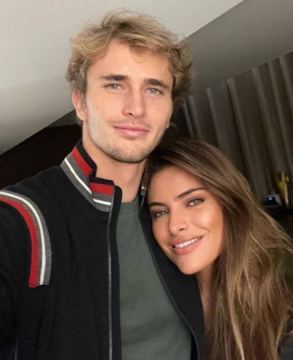 Alexander Zverev und Sophia Thomalla blicken in die Kamera und lächeln. Sie legt ihren Kopf auf seine Brust.