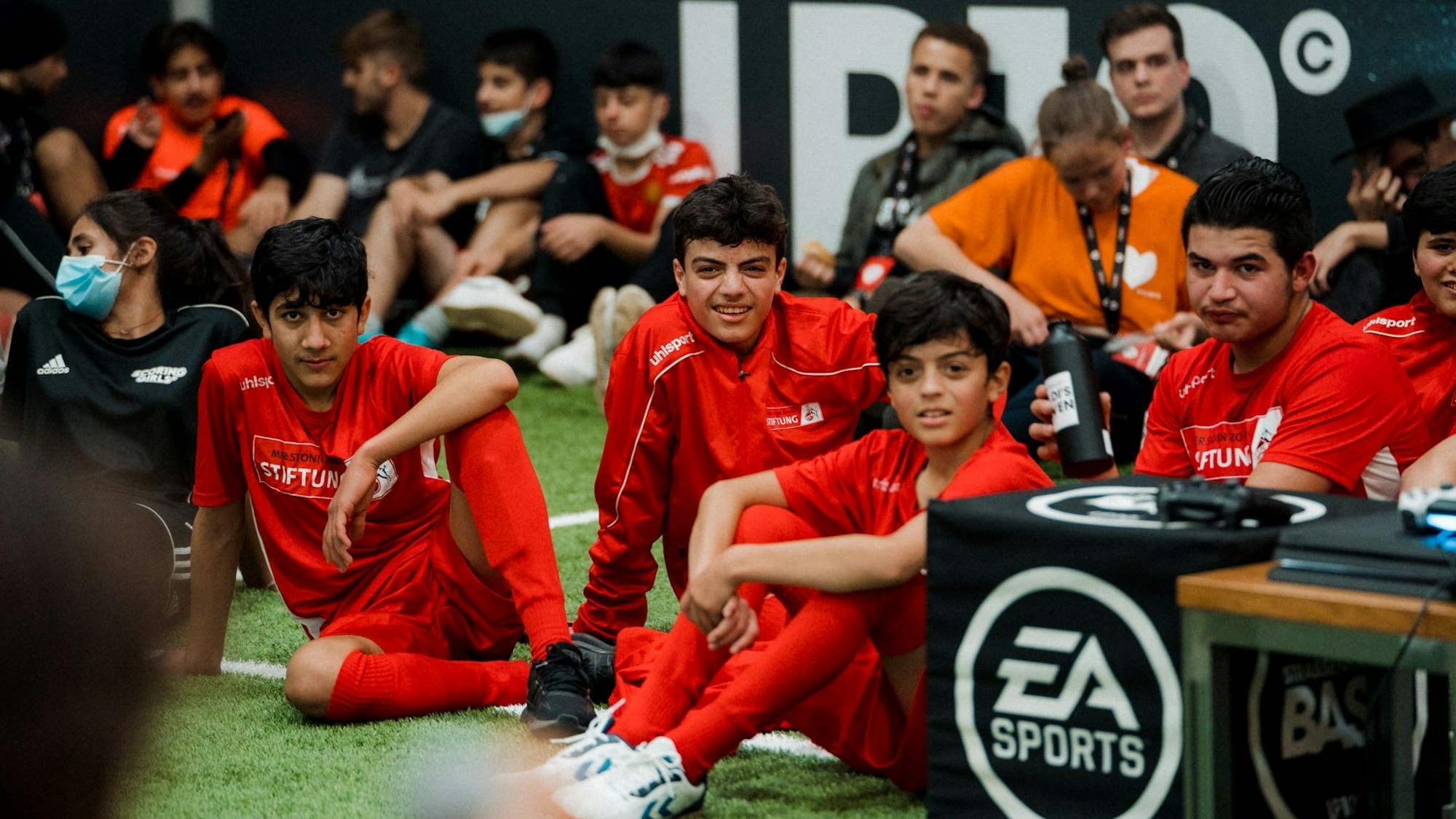 Junge Hobbykicker sitzen in der Straßenkicker-Base auf dem Kunstrasen.