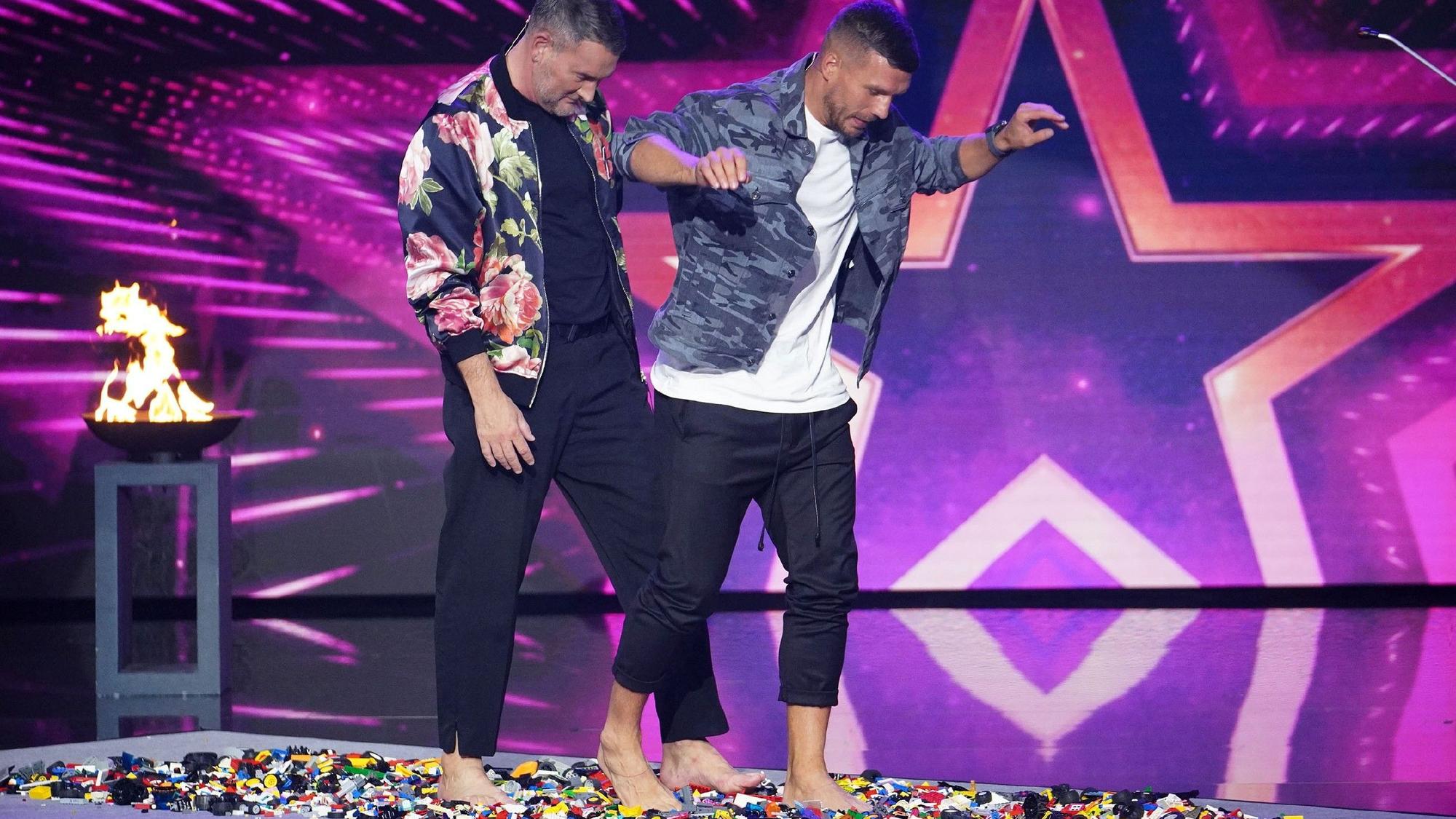 Die Jurymitglieder Michael Michalsky (l.) und Lukas Podolski wagen sich barfuß über die Lego-Steine von Francesco Infantone.