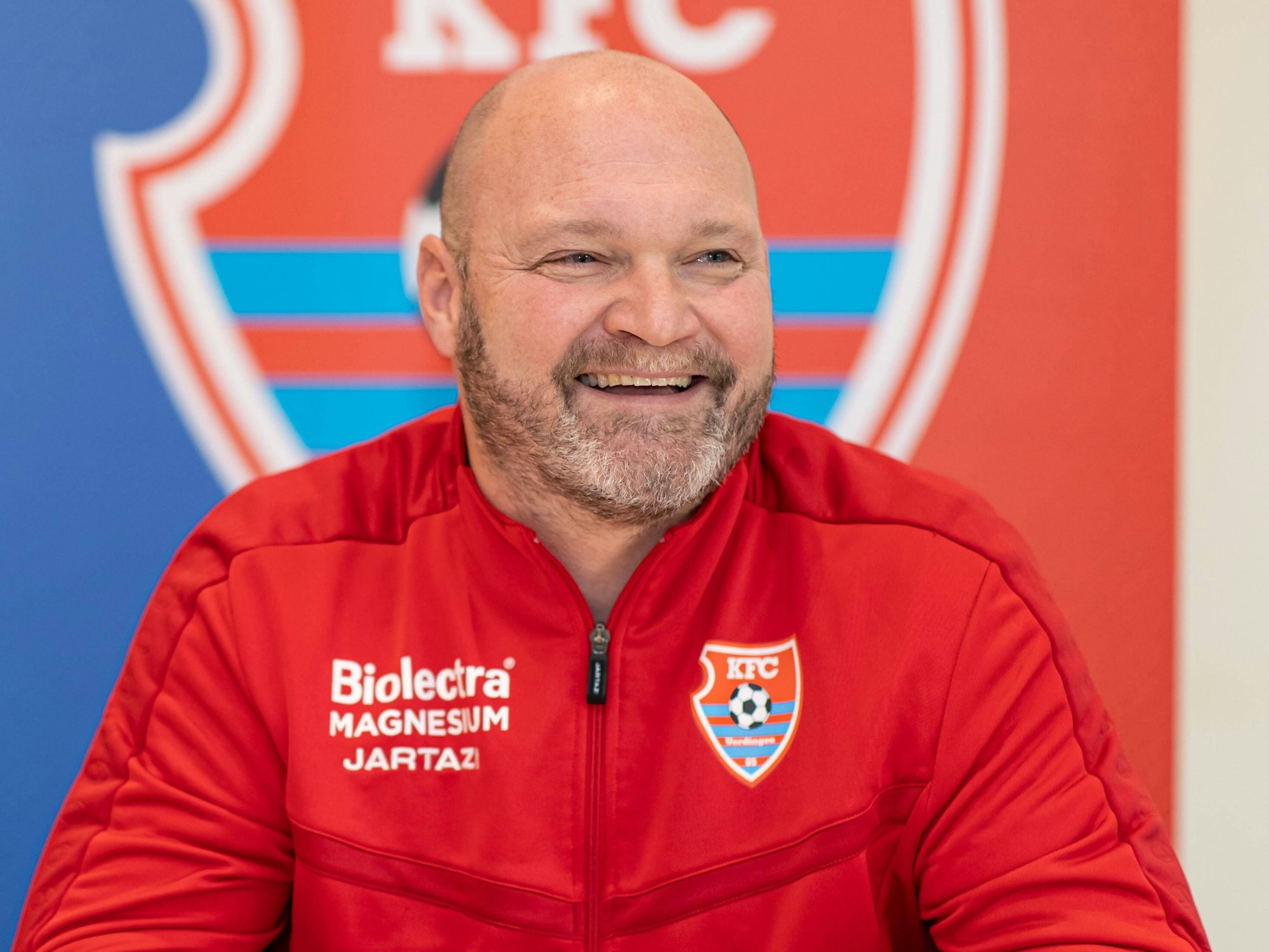 Alexander Voigt sitzt auf der Pressekonferenz und trägt ein Trainingsanzug des KFC.