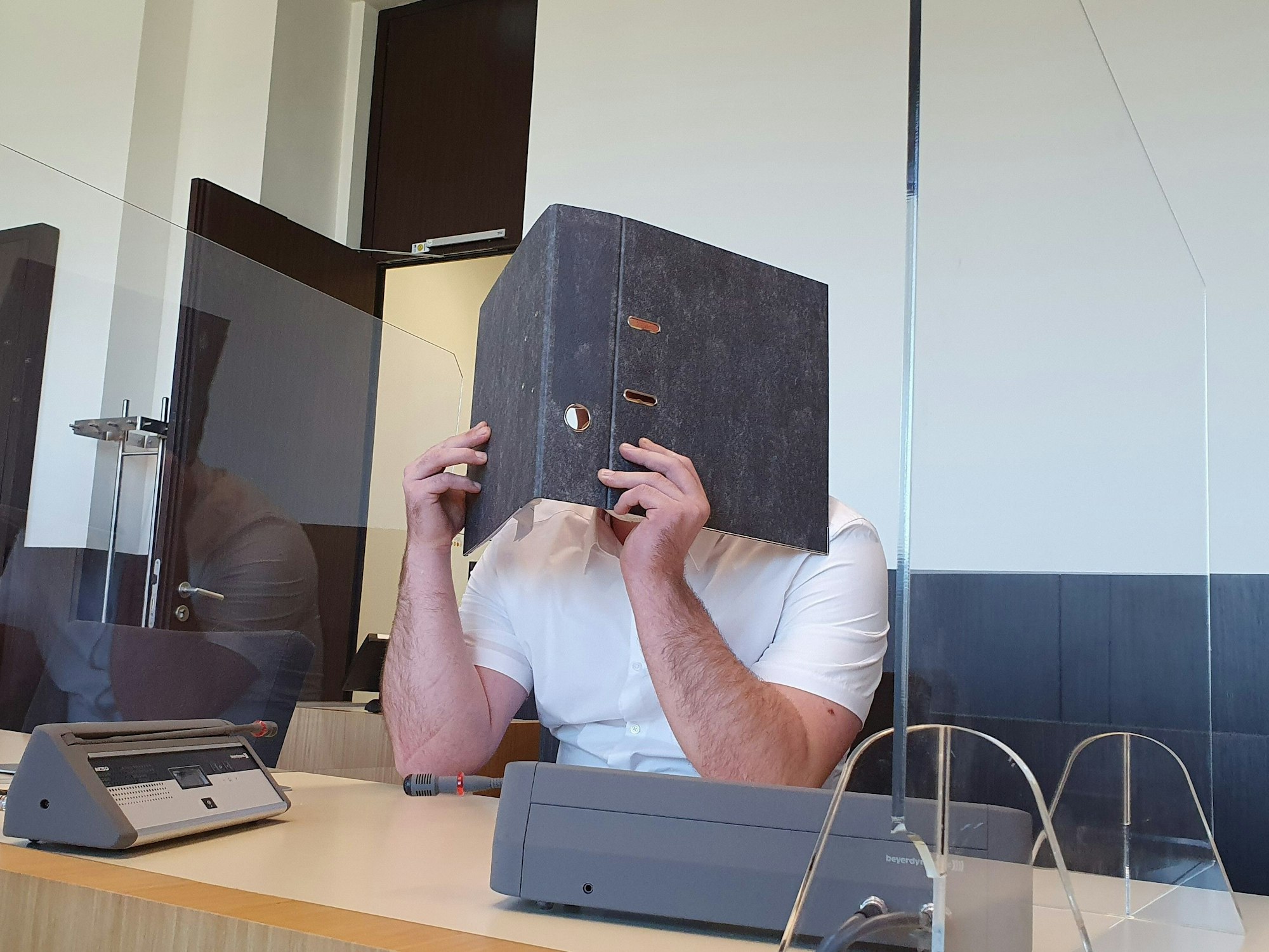 Der Angeklagte sitzt im Gerichtssaal und verdeckt sein Gesicht.