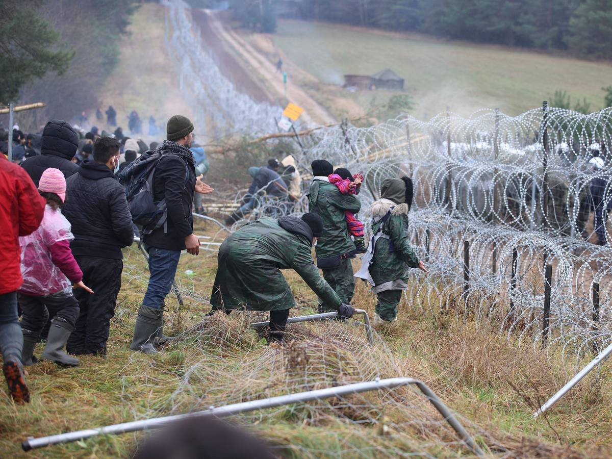 Migranten, die in Belarus vor der Grenze zu Polen festsitzen, stehen am 8. November vor Stacheldraht, auf der anderen Seite stehen Soldaten.