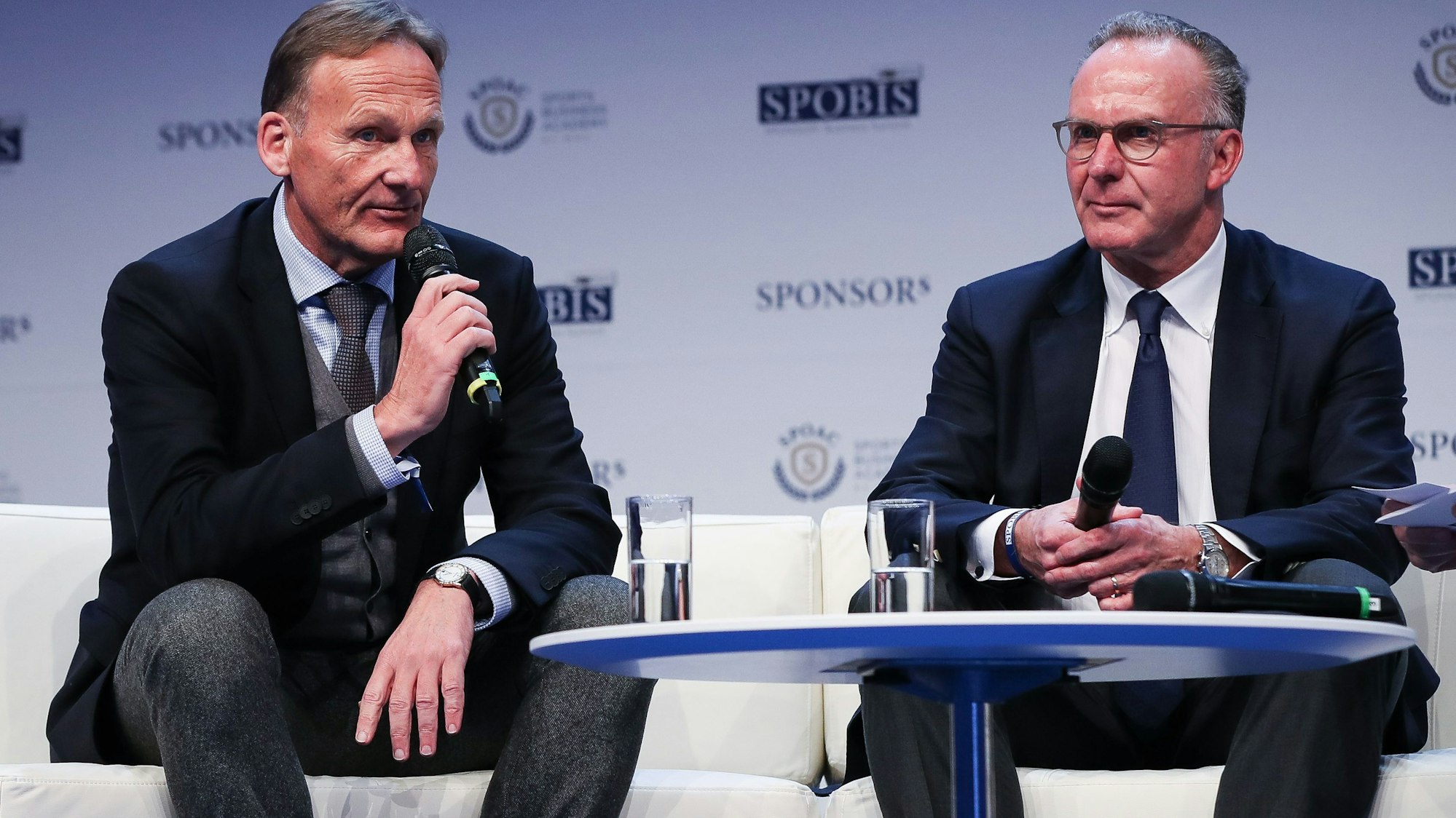 Karl-Heinz Rummenigge (r.) und Hans-Joachim Watzke sitzen nebeneinander auf der Bühne.