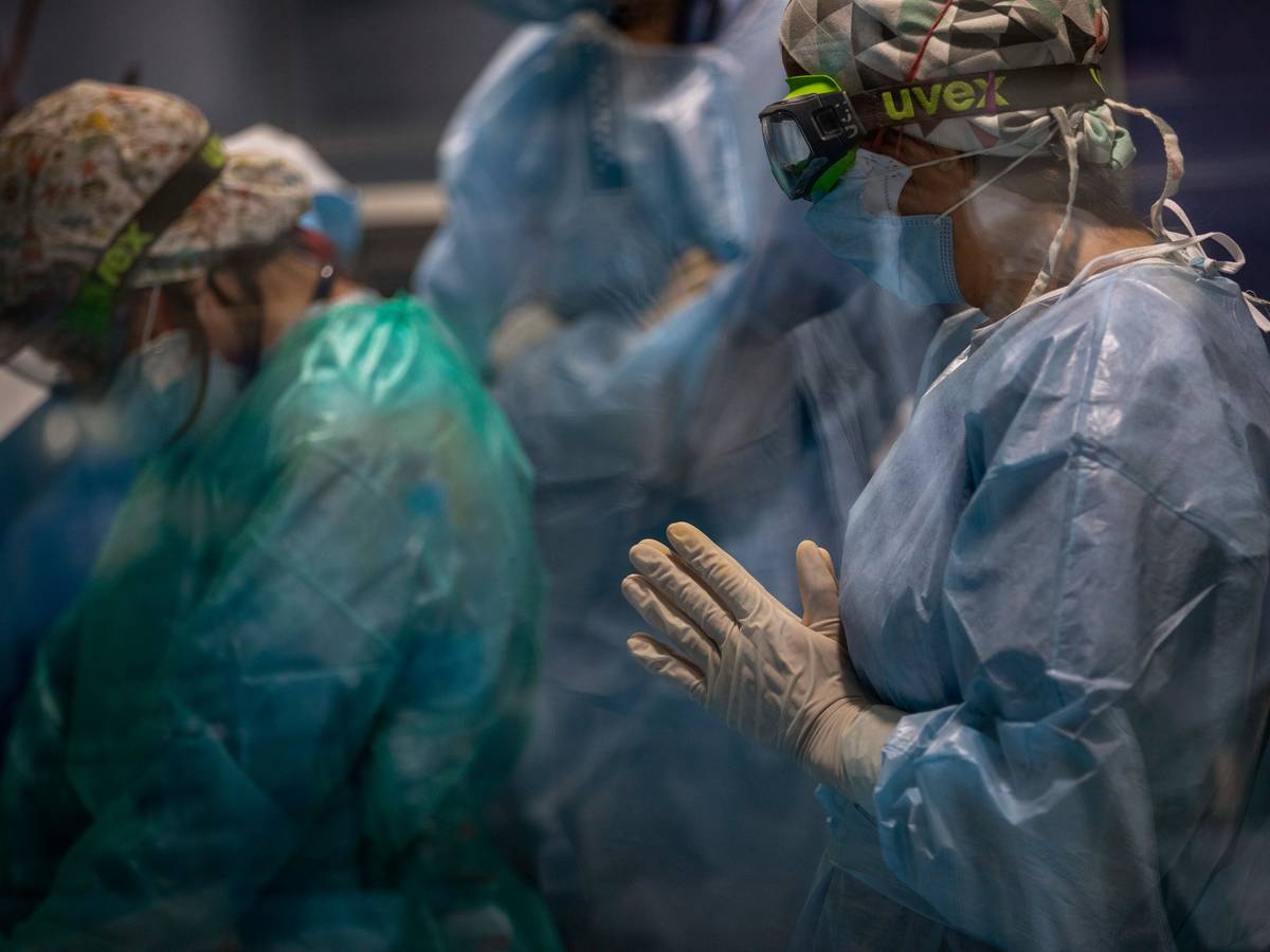 Ein Mitarbeiter des Gesundheitswesens mit doppelter Maske und einer Uvex-Brille schaut zu, wie ein Team bei einem Covid-19-Patienten auf der Intensivstation des Hospital del Mar einen Luftröhrenschnitt durchführt.