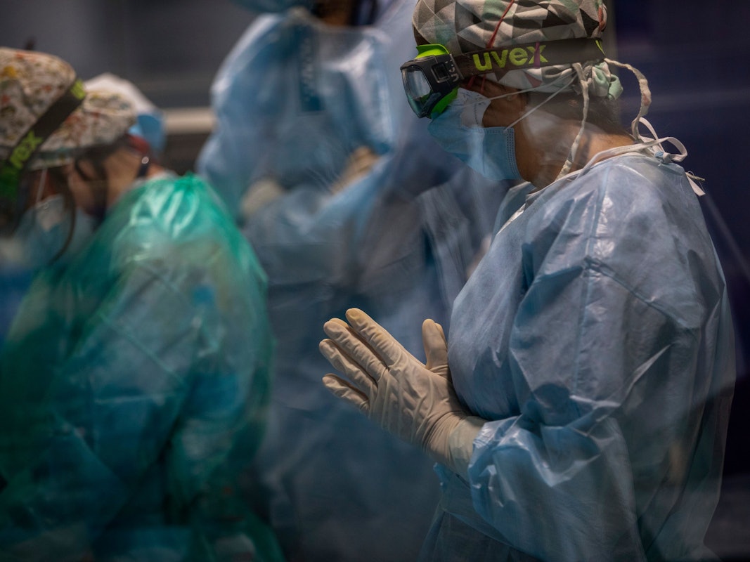 Ein Mitarbeiter des Gesundheitswesens mit doppelter Maske und einer Uvex-Brille schaut zu, wie ein Team bei einem Covid-19-Patienten auf der Intensivstation des Hospital del Mar einen Luftröhrenschnitt durchführt.