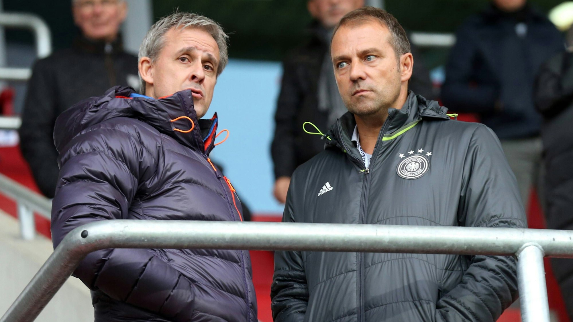 Pierre Littbarski und Hansi Flick stehen gemeinsam auf der Tribüne.