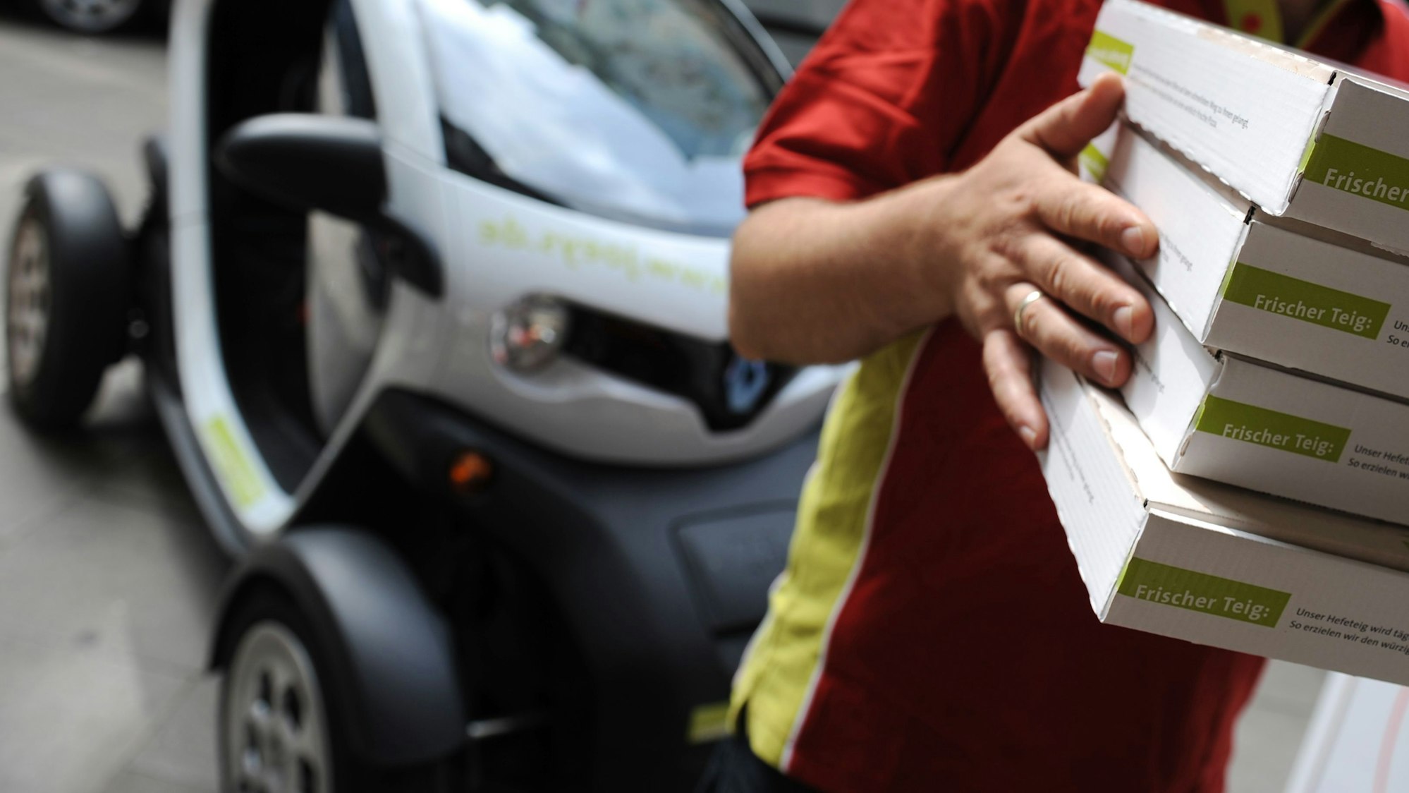 Ein Pizza-Lieferant hält am 21.08.2012 in Hamburg vor einem Elektrofahrzeug mehrere Pizzaschachteln.