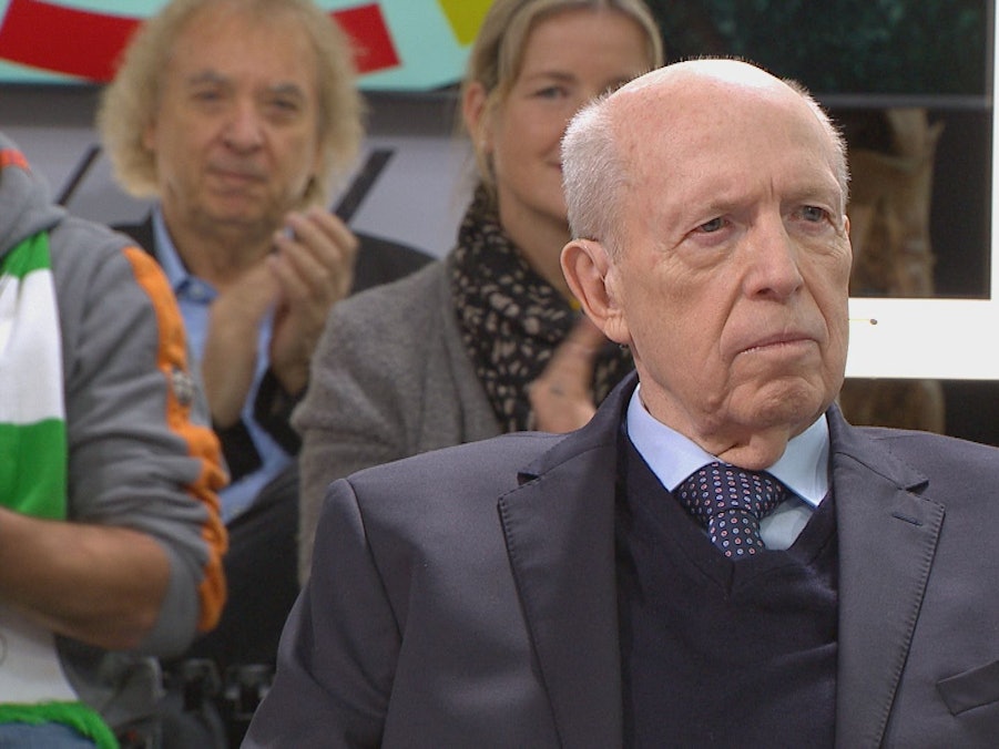 Reiner Calmund sitzt auf einem Stuhl, im Hintergrund sitzen Zuschauer.