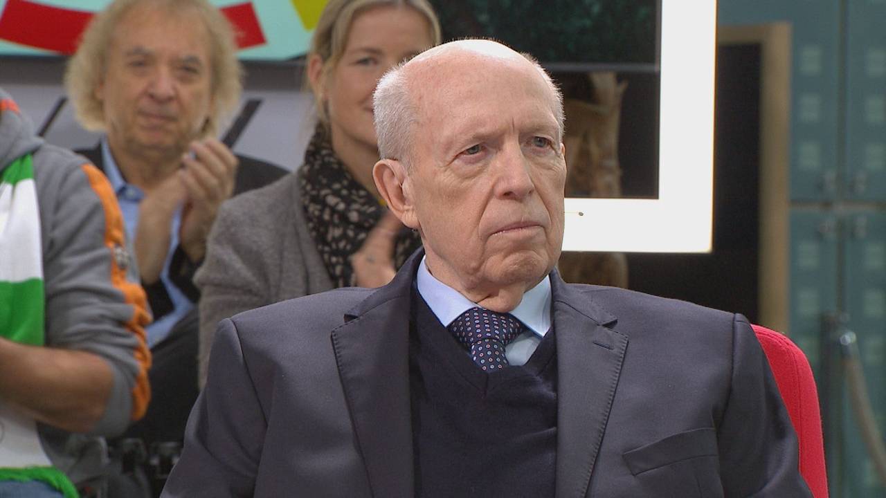 Reiner Calmund sitzt auf einem Stuhl, im Hintergrund sitzen Zuschauer.