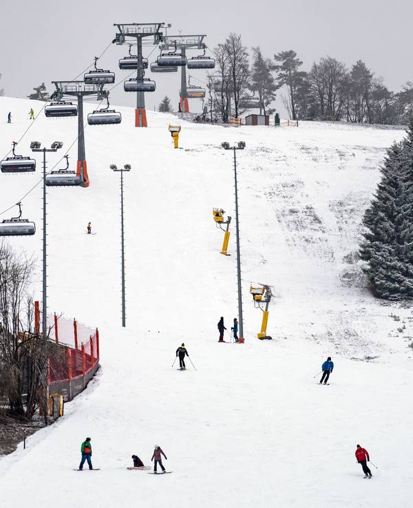 Wintersportler und -sportlerinnen auf Skiern und Snowboards fahren am Ettelsberg im Sauerland eine Abfahrt hinunter.