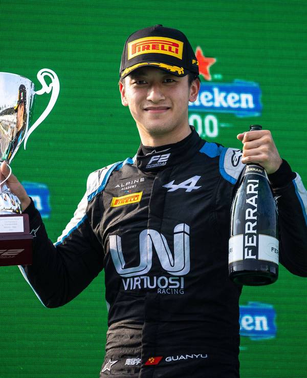 Guanyu Zhou hält einen Pokal und eine Ferrari-Flasche nach oben.