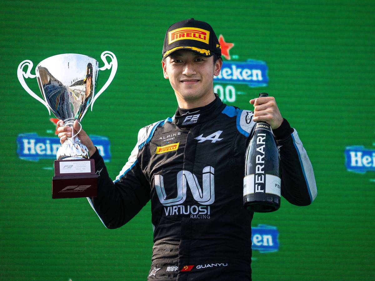 Guanyu Zhou hält einen Pokal und eine Ferrari-Flasche nach oben.