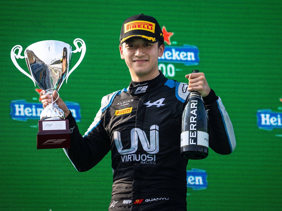 Guanyu Zhou hält einen Pokal und eine Ferrari-Flasche nach oben.