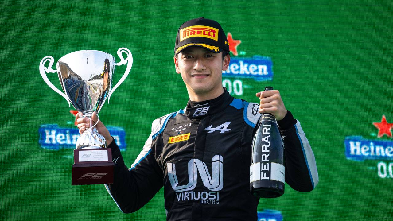 Guanyu Zhou hält einen Pokal und eine Ferrari-Flasche nach oben.