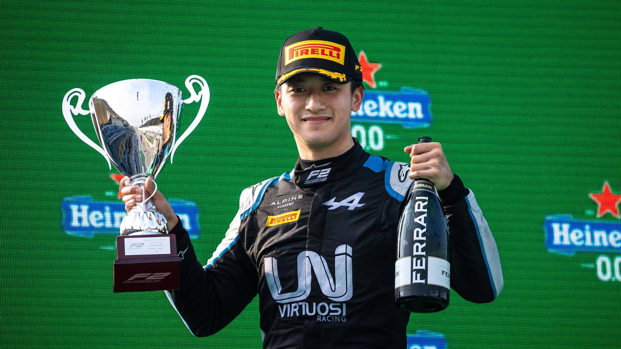 Guanyu Zhou hält einen Pokal und eine Ferrari-Flasche nach oben.